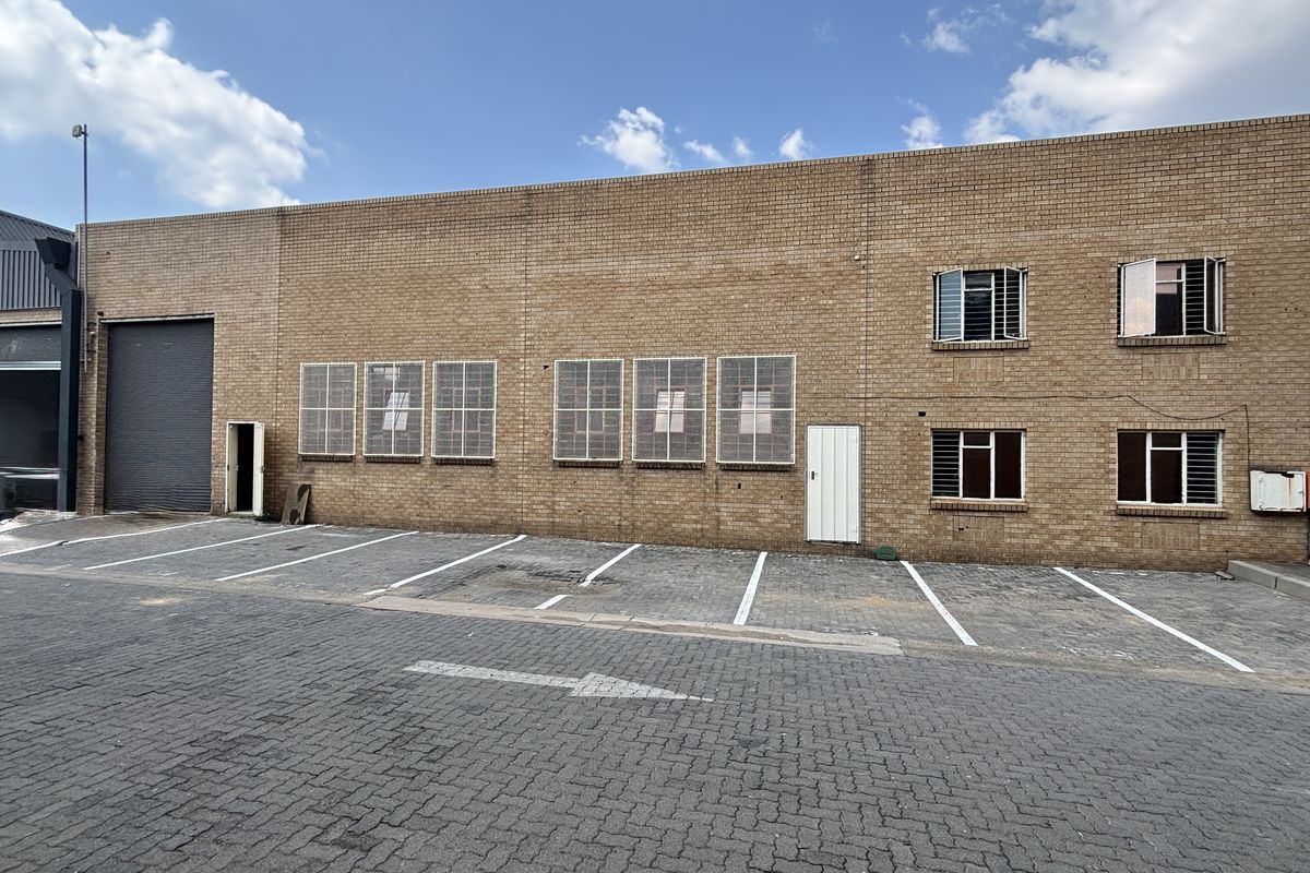 Industrial property exterior featuring a face brick facade, roller shutter door, and dedicated paved parking bays with security-fitted windows.