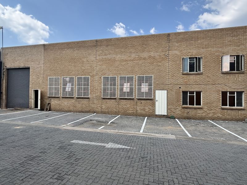 Industrial property exterior featuring a face brick facade, roller shutter door, and dedicated paved parking bays with security-fitted windows.