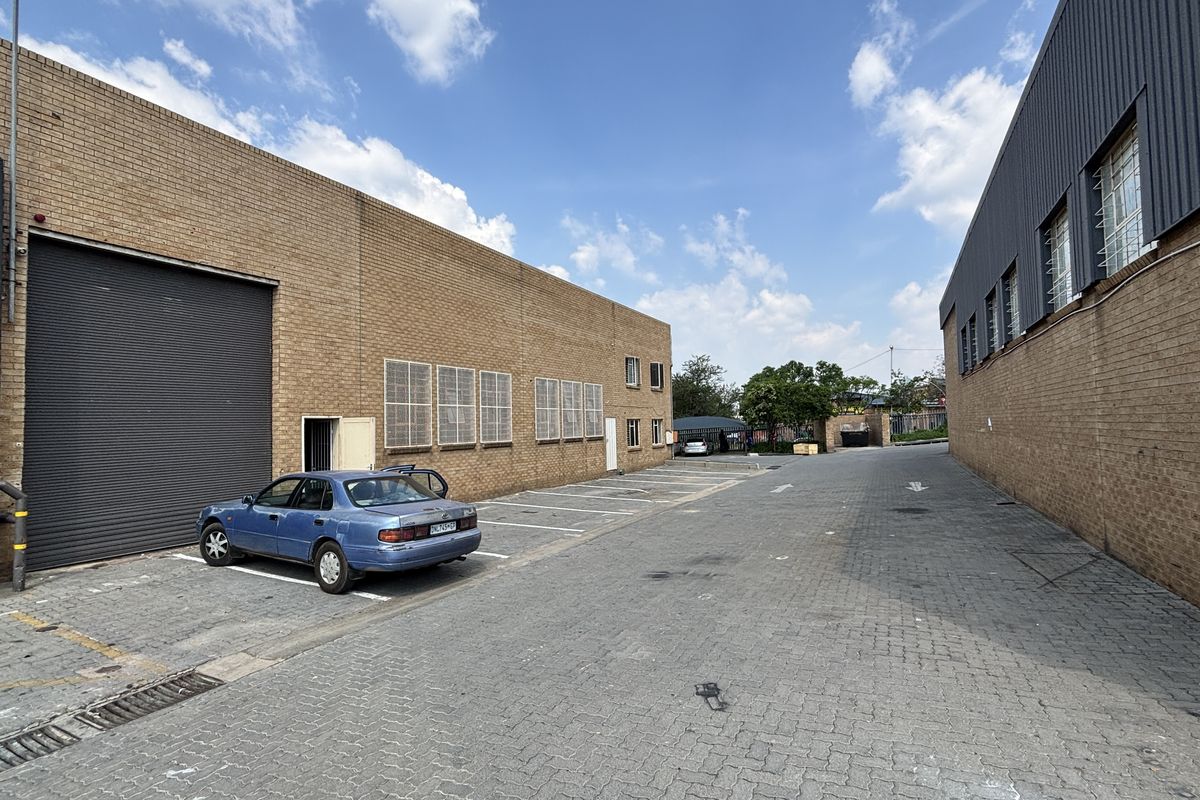 Industrial exterior view featuring a paved driveway, brick facade, and a large roller shutter door for loading access.