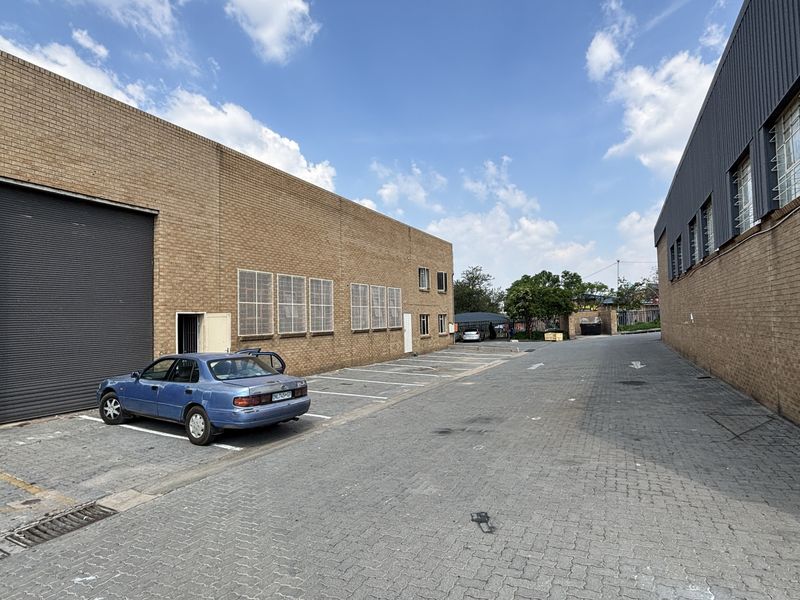 Industrial exterior view featuring a paved driveway, brick facade, and a large roller shutter door for loading access.