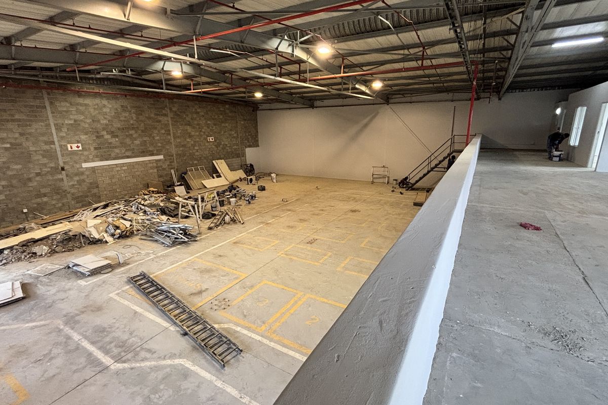 Spacious industrial warehouse unit featuring high ceilings with exposed steel trusses, concrete flooring, a mezzanine level, and integrated fire sprinkler system.