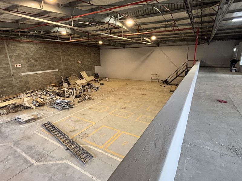 Spacious industrial warehouse unit featuring high ceilings with exposed steel trusses, concrete flooring, a mezzanine level, and integrated fire sprinkler system.