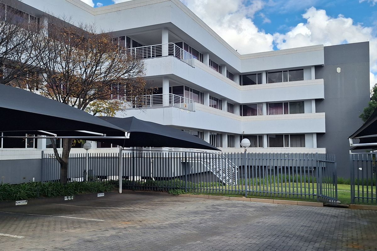 Exterior view of a multi-story office building featuring a paved parking area with shade cloth carports and secure perimeter fencing.