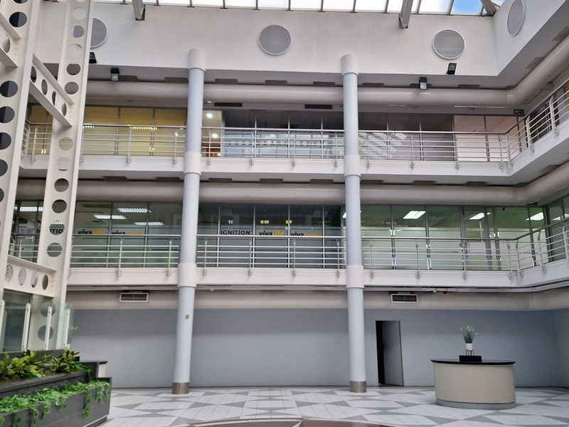 Spacious office building atrium featuring a large glass skylight, multi-level mezzanine walkways with steel balustrades, and a central tiled floor design.
