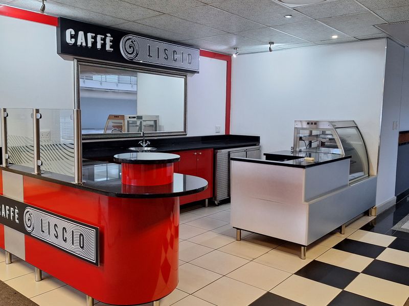 A modern, well-maintained office coffee station featuring a built-in service counter, display cabinet, sink, and professional tiled flooring.