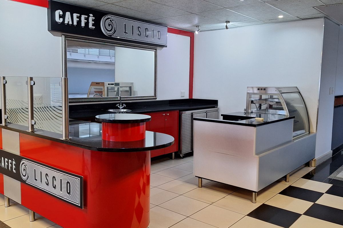A modern, well-maintained office coffee station featuring a built-in service counter, display cabinet, sink, and professional tiled flooring.