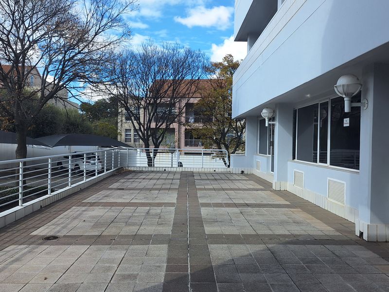 A spacious, paved outdoor terrace area featuring metal safety railings and wall-mounted exterior lighting, suitable for office break-out space.