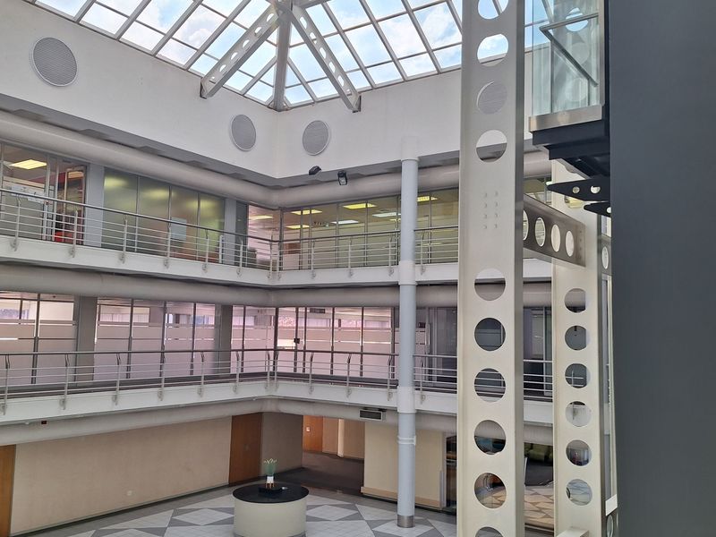 Spacious multi-level office atrium featuring a large glass skylight, modern steel structural elements, and open mezzanine walkways overlooking the central lobby area.