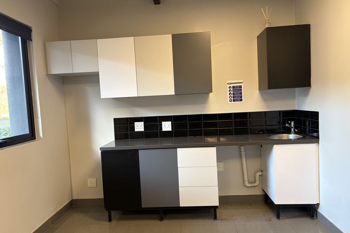 A functional kitchenette area featuring modern two-tone cabinetry, a dark countertop, black tiled splashback, and a stainless steel sink.