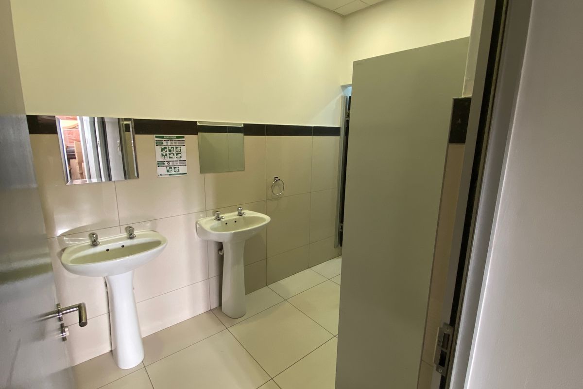 A clean, functional industrial restroom featuring two pedestal basins, tiled walls, and tiled flooring.