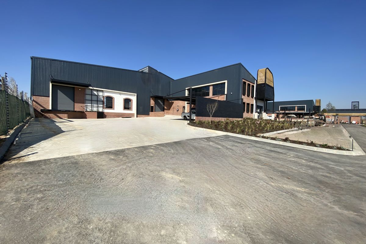 Modern industrial facility featuring metal cladding, brick accents, a large roller shutter door, and a spacious concrete loading area with landscaped surroundings.