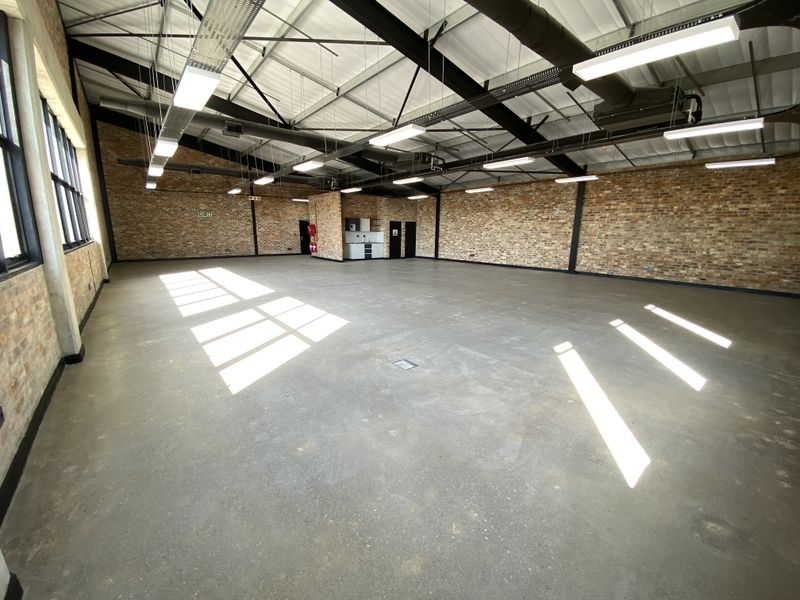Spacious open-plan industrial unit featuring polished concrete floors, exposed brick walls, high ceilings with steel trusses, and integrated linear lighting.