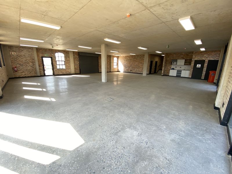 Spacious open-plan industrial unit featuring polished concrete floors, exposed brick walls, high ceilings, and a functional kitchenette area.