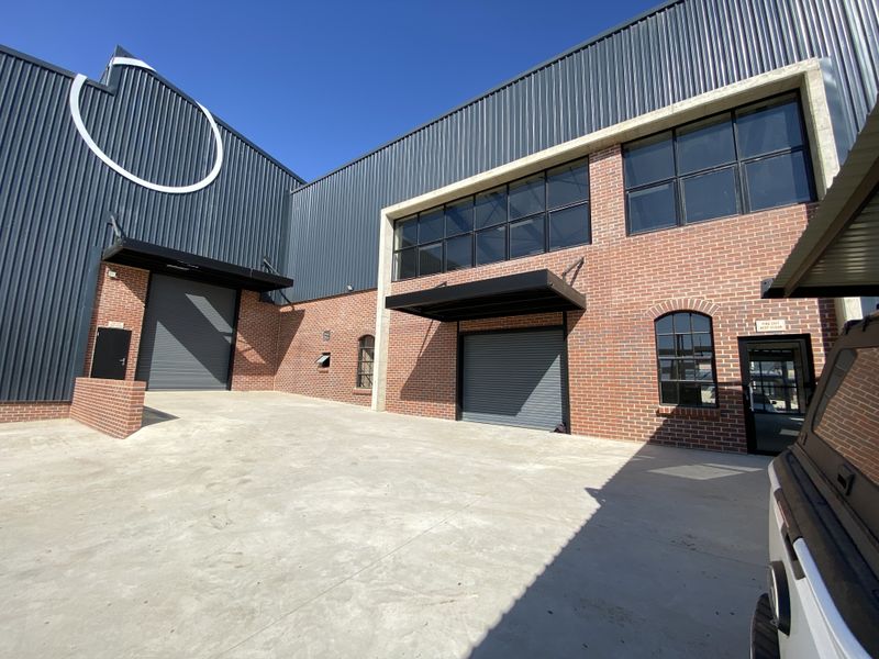 Modern industrial facility featuring a combination of corrugated metal cladding and face brick facade with multiple roller shutter doors and concrete driveway access.