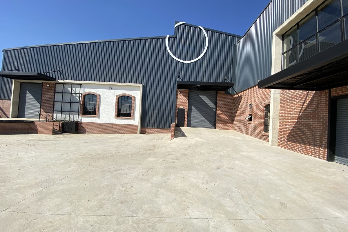 Modern industrial facility featuring a spacious concrete yard, loading dock access, and a combination of corrugated metal and exposed brick exterior finishes.