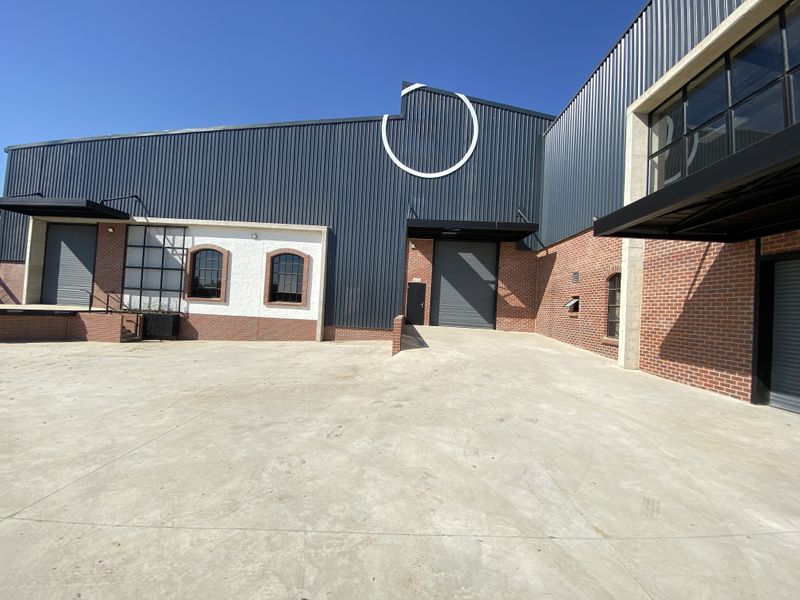 Modern industrial facility featuring a spacious concrete yard, loading dock access, and a combination of corrugated metal and exposed brick exterior finishes.
