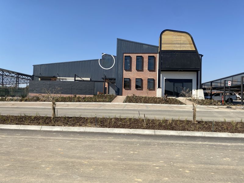 Modern industrial building facade featuring a combination of dark metal cladding, exposed brickwork, and contemporary architectural timber detailing with a paved entrance.
