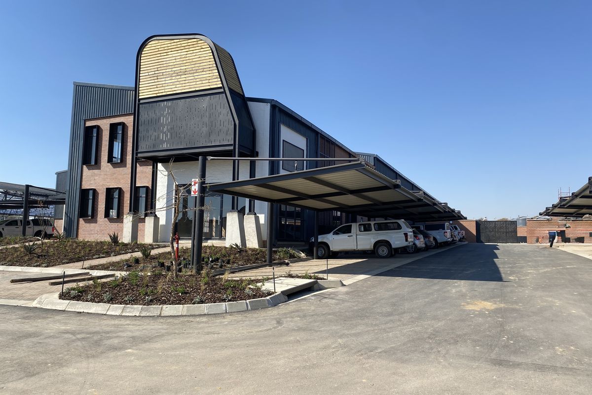 Modern industrial office building featuring a striking architectural entrance, covered parking bays, and neatly landscaped garden beds on a paved site.