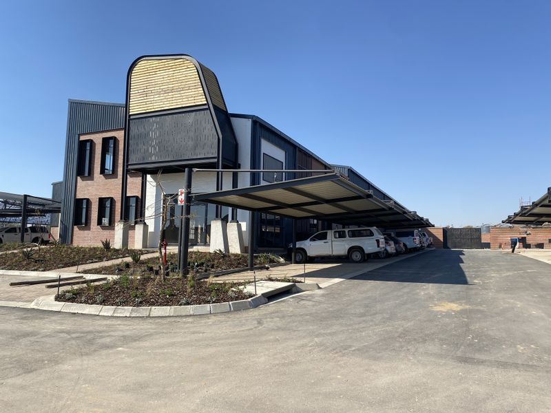 Modern industrial office building featuring a striking architectural entrance, covered parking bays, and neatly landscaped garden beds on a paved site.