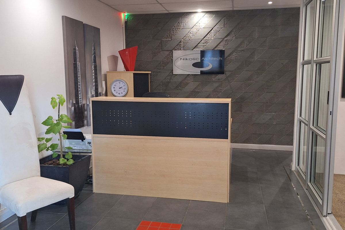 Professional office reception area featuring a built-in reception desk, textured stone feature wall, and modern tiled flooring with glass partition access.