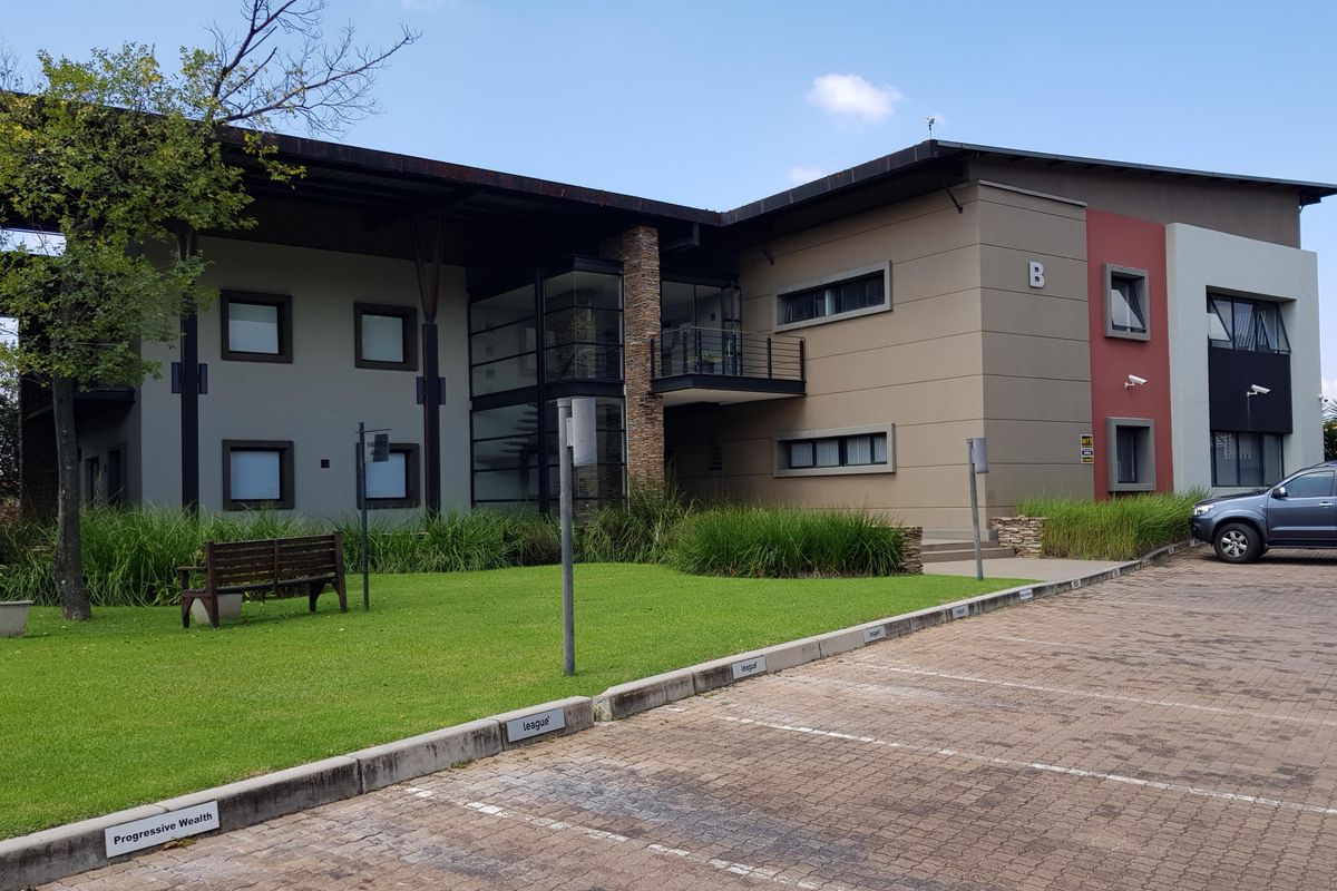 Modern office building exterior featuring a multi-level facade with stone accents, integrated security cameras, and a paved parking area with landscaped grounds.