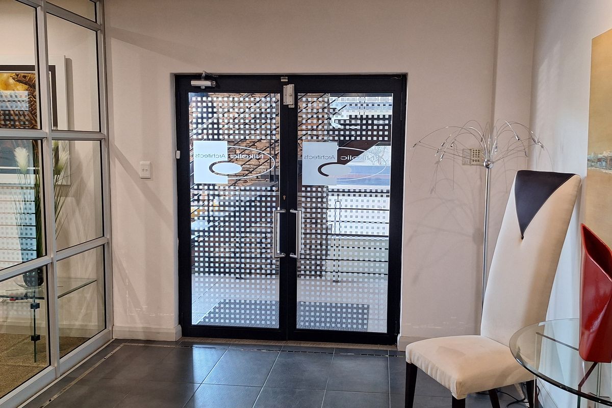 A professional office entrance featuring double glass doors, tiled flooring, and a modern glass partition wall, creating a bright and welcoming reception area.