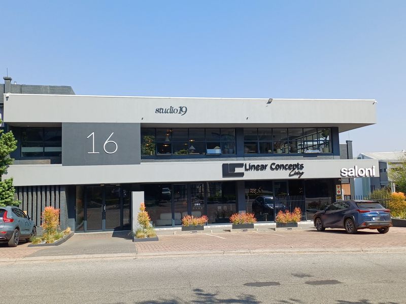 A modern commercial retail building facade featuring large glass windows, paved parking area, and prominent signage for studio 19 and Linear Concepts.