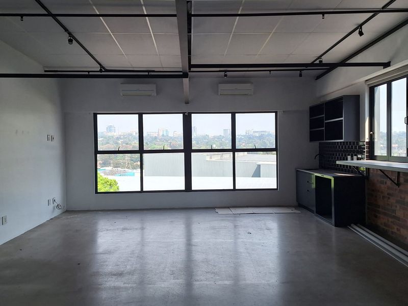Spacious open-plan commercial unit featuring polished concrete floors, exposed track lighting, split-system air conditioning, and a modern kitchenette with subway tile backsplash.