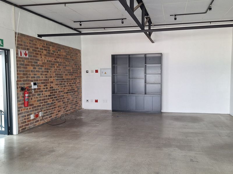 Spacious open-plan retail area featuring polished concrete floors, exposed steel trusses, track lighting, and a characterful exposed brick feature wall.