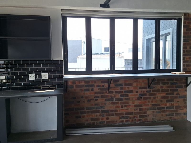 A modern kitchen area featuring exposed brickwork, black subway tile backsplash, built-in cabinetry, and a convenient window-side breakfast bar.