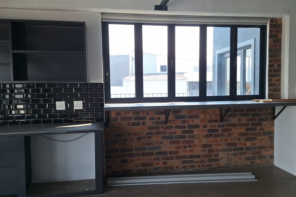 A modern kitchen area featuring exposed brickwork, black subway tile backsplash, built-in cabinetry, and a convenient window-side breakfast bar.