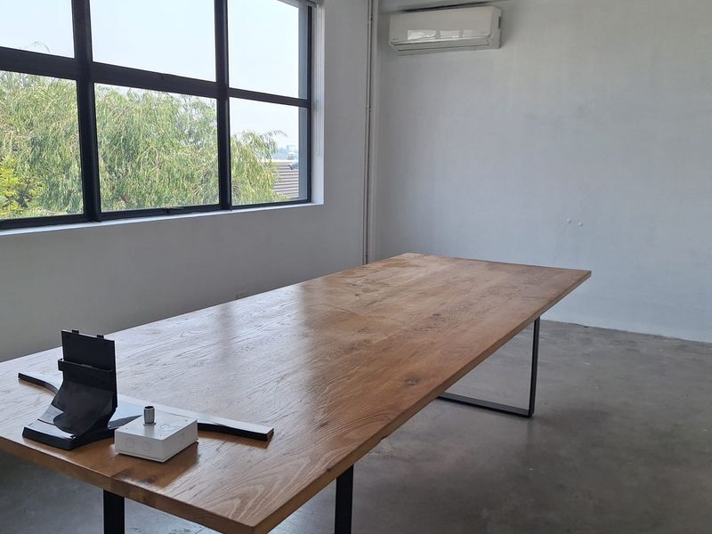 A bright, modern office space featuring polished concrete floors, a large industrial window, and a wall-mounted air conditioning unit.