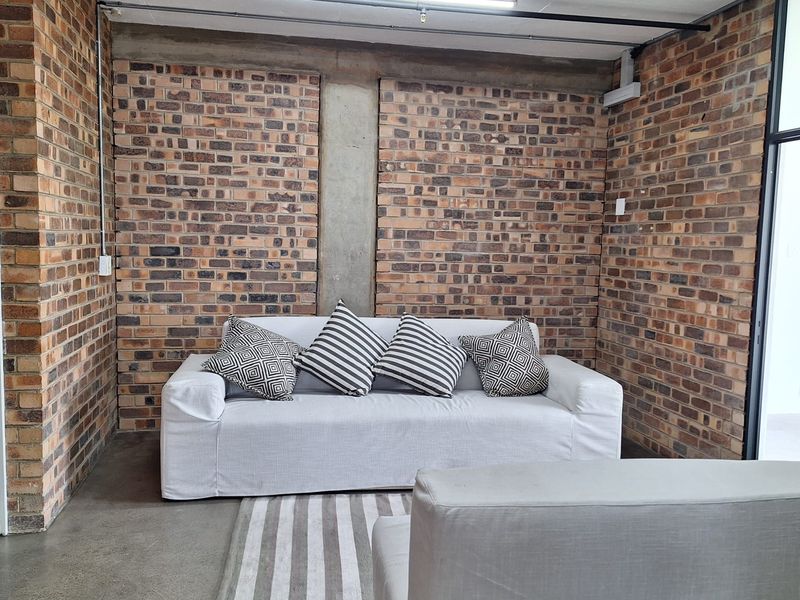 A modern industrial-style living area featuring exposed brick walls, polished concrete flooring, and a raw concrete ceiling with strip lighting.