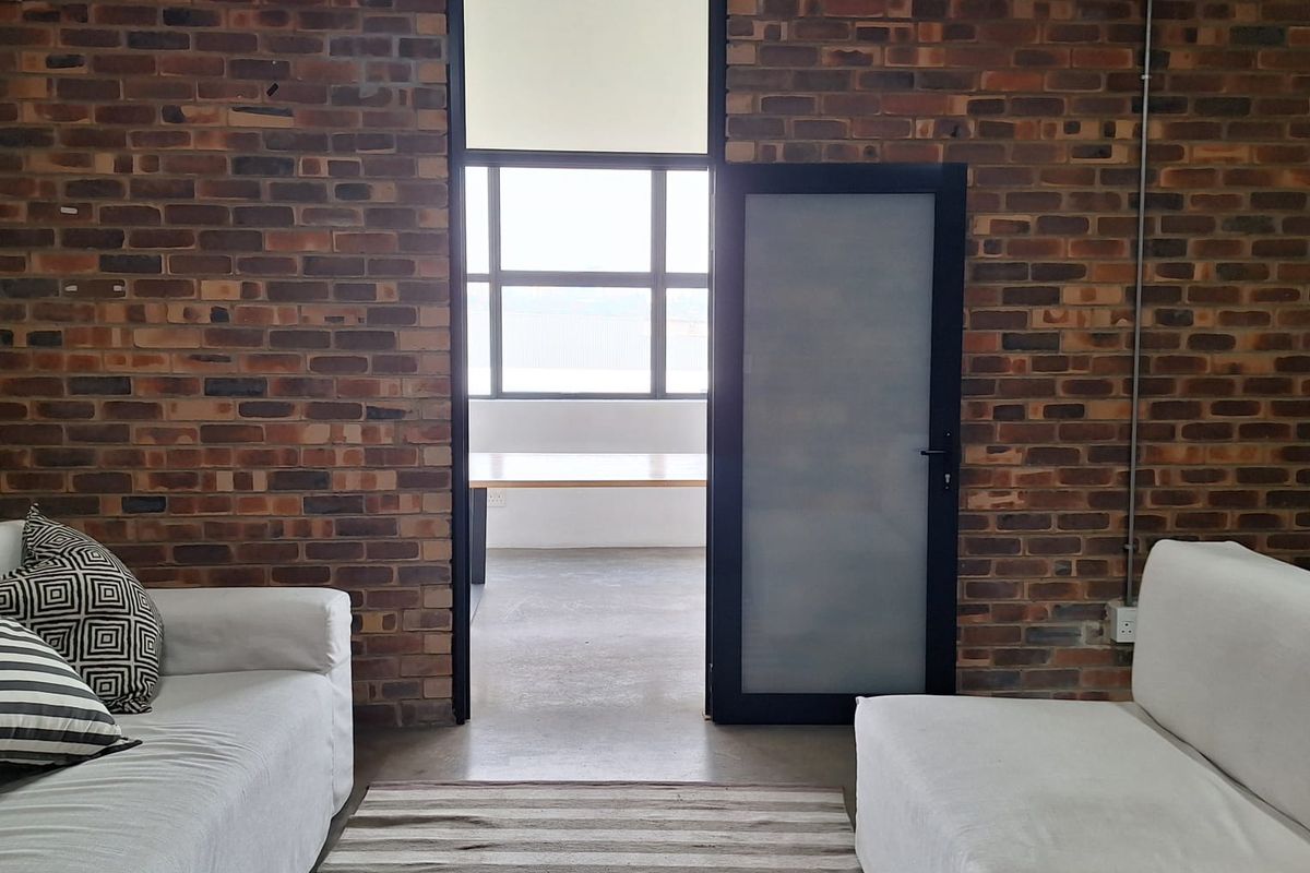 A contemporary living space featuring industrial-style exposed brick walls, concrete flooring, and a frosted glass door leading to an adjacent room.