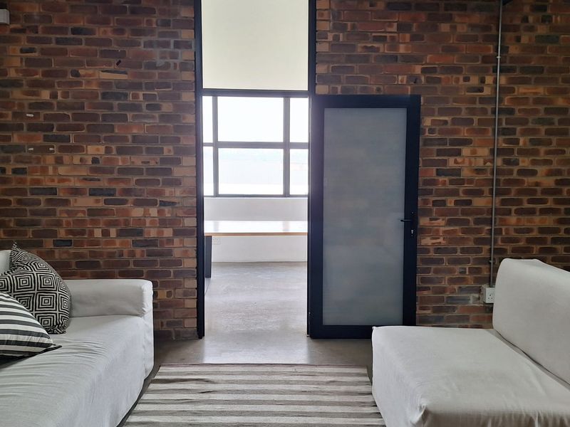 A contemporary living space featuring industrial-style exposed brick walls, concrete flooring, and a frosted glass door leading to an adjacent room.