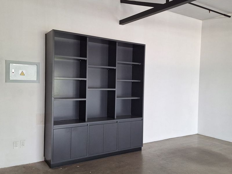 An open-plan retail space featuring polished concrete floors, exposed ceiling beams, and a large built-in dark grey storage unit.