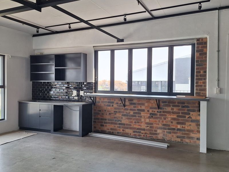 Modern industrial-style kitchenette featuring exposed ceiling beams, track lighting, polished concrete floors, and a brick-accented breakfast bar with built-in cabinetry.