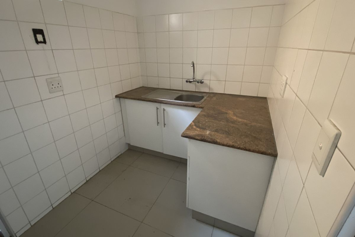 A functional kitchenette area featuring white cabinetry, a stone-look countertop, a stainless steel sink, and full-height wall tiling.