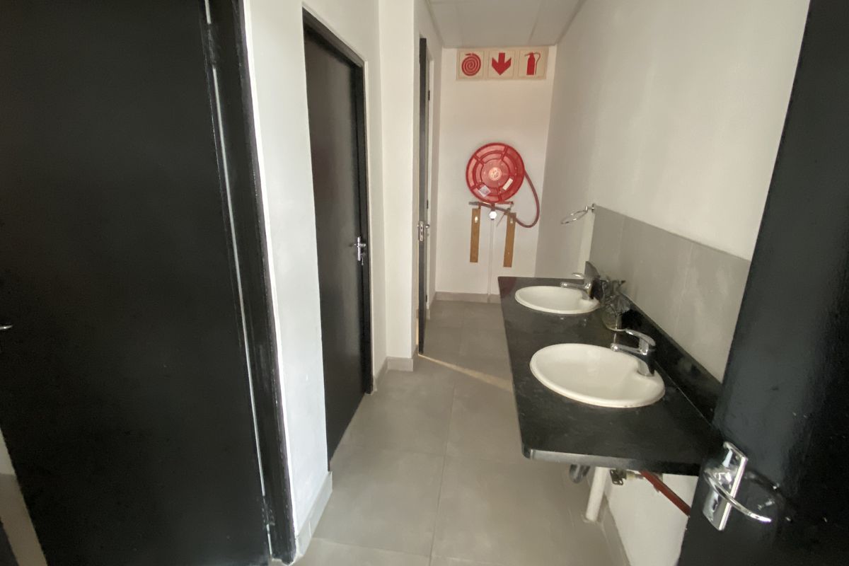 A functional industrial washroom area featuring a dual-basin vanity with granite countertop, tiled flooring, and wall-mounted fire safety equipment.