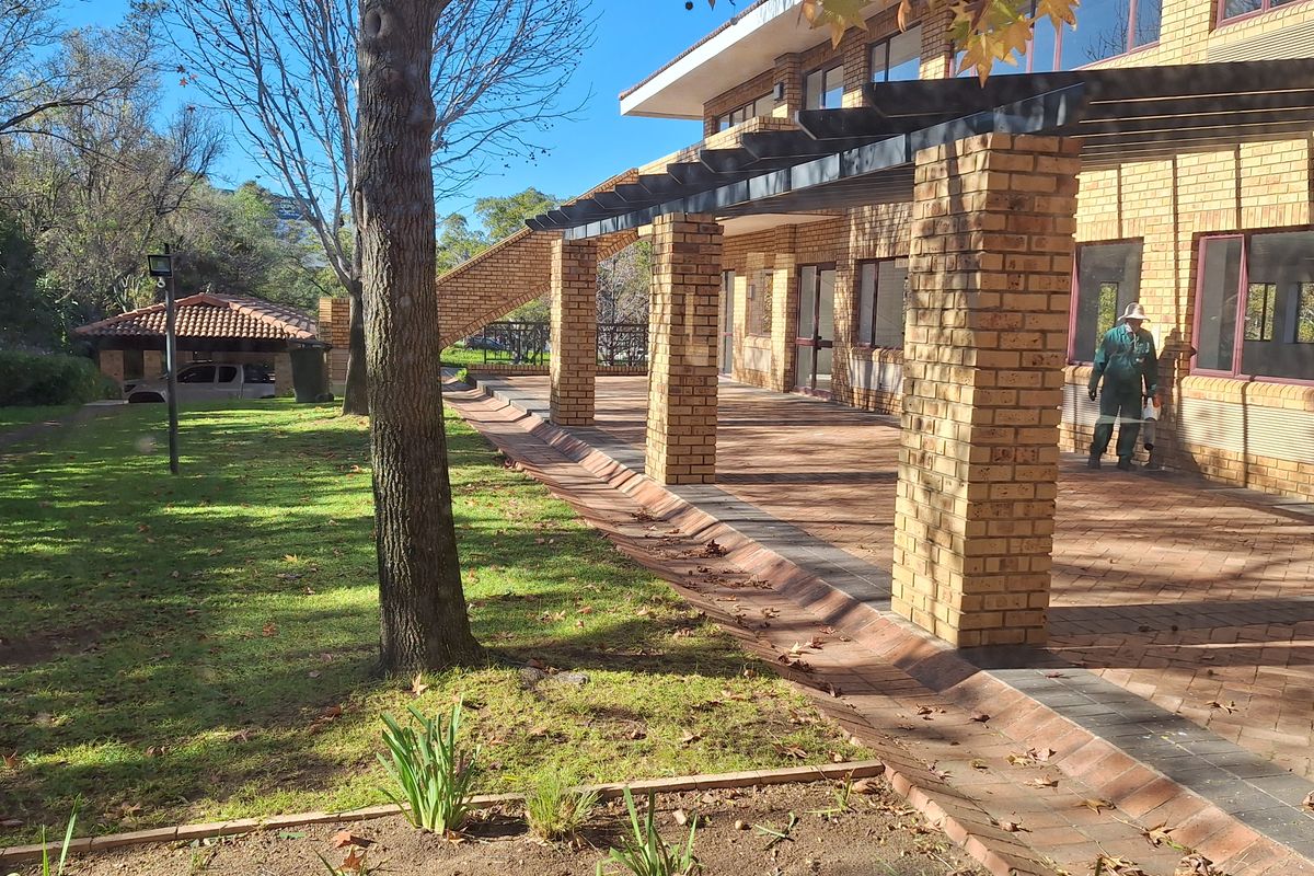 A well-maintained office exterior featuring a spacious brick-paved patio with pergola, overlooking a landscaped garden area.