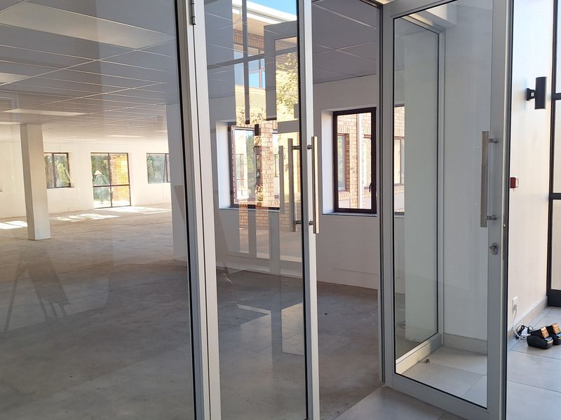 A bright, open-plan office space featuring modern glass partition doors, a suspended ceiling, and neutral tiled flooring, ready for custom fit-out.