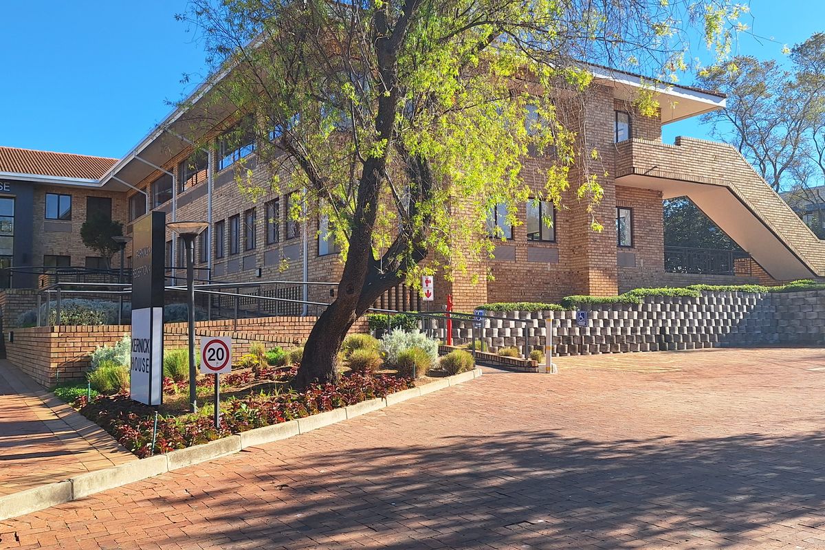 Front exterior view of a multi-story brick office building featuring a paved driveway, landscaped garden beds, and an external staircase.