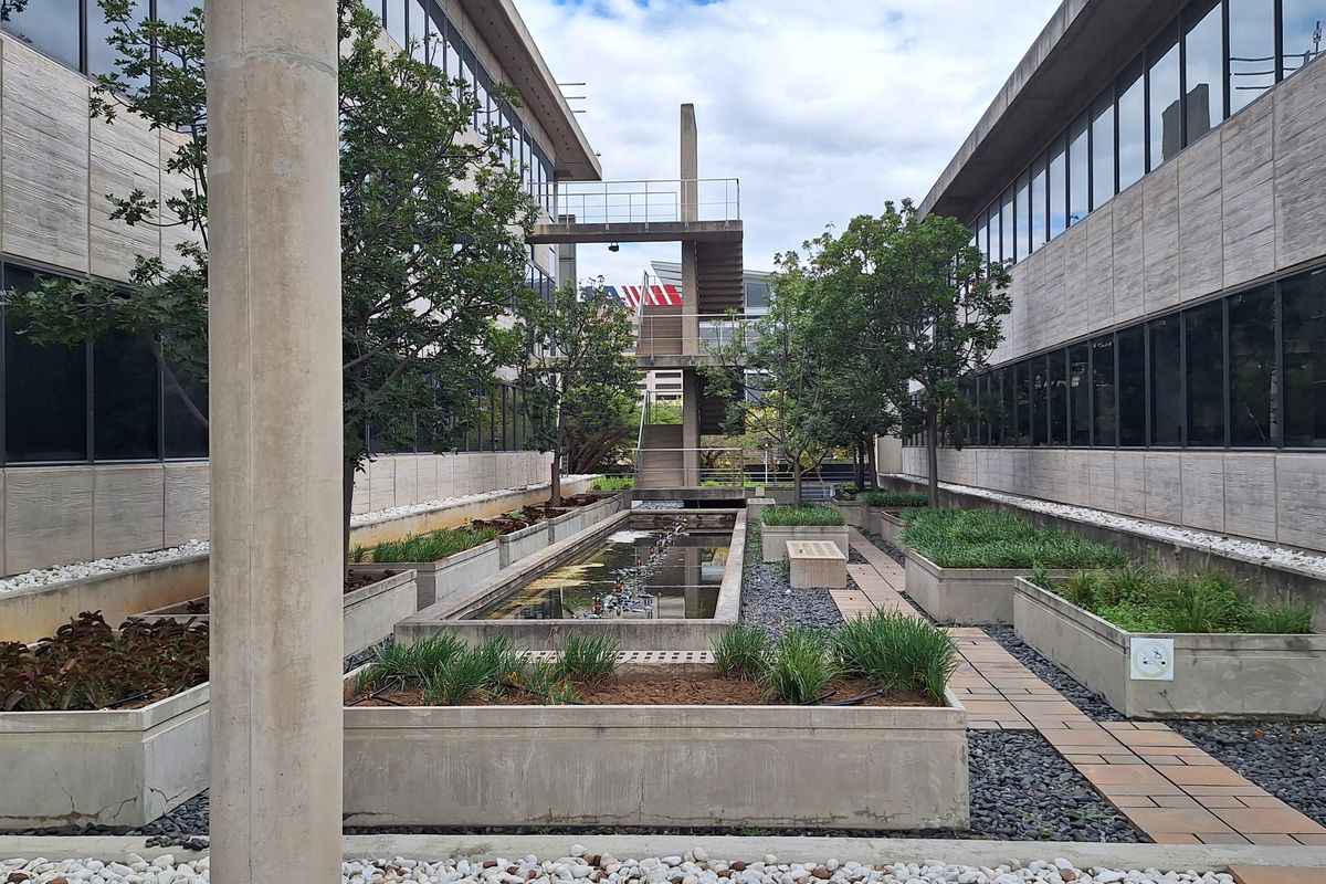 A modern office courtyard featuring landscaped concrete planters, a central water feature, and an external metal staircase connecting the building wings.