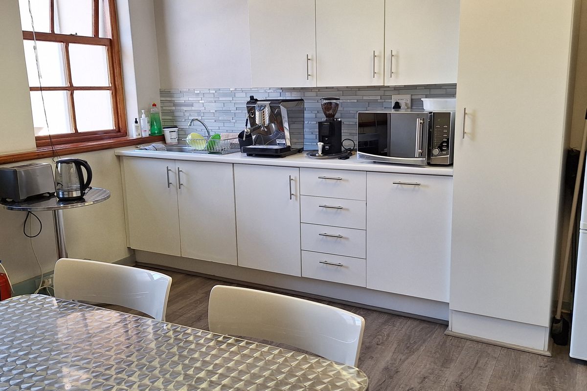 A functional office kitchenette featuring white cabinetry, a tiled backsplash, a stainless steel sink, and wood-look flooring.