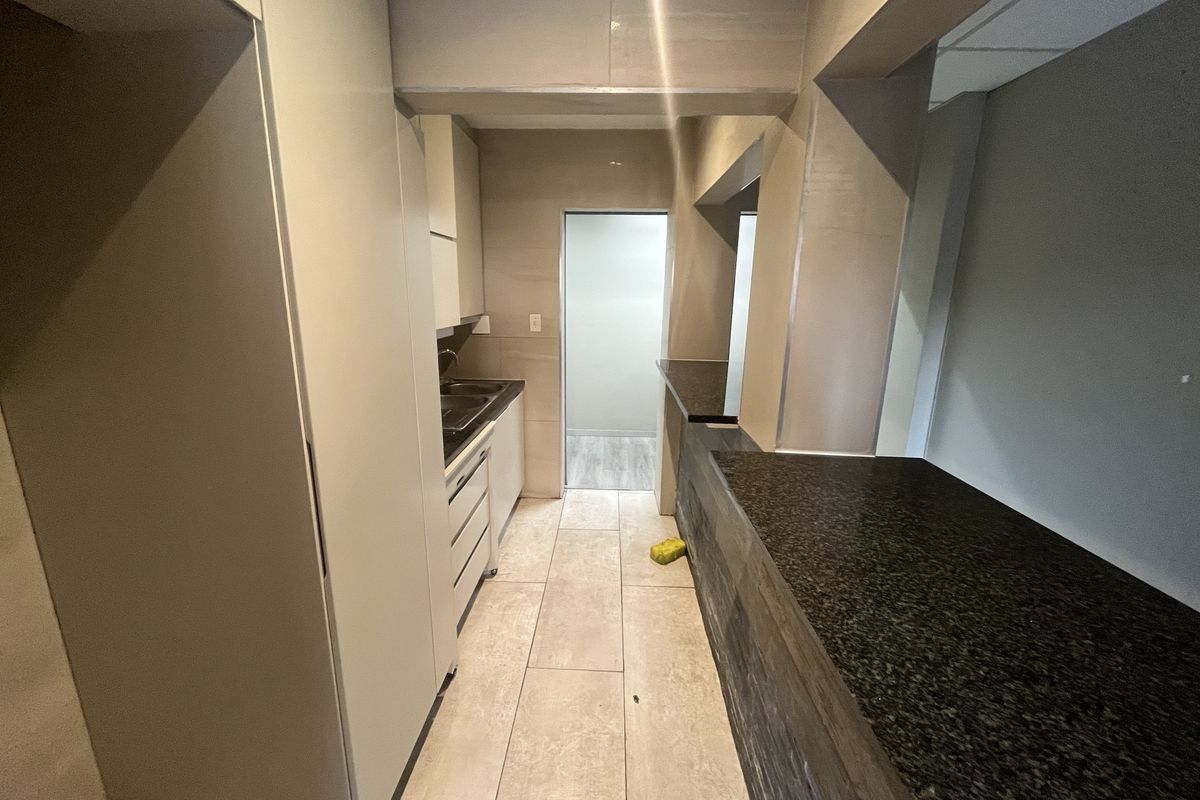 A functional office kitchenette featuring built-in cabinetry, a dark granite countertop, and tiled flooring, providing a clean and efficient workspace utility area.