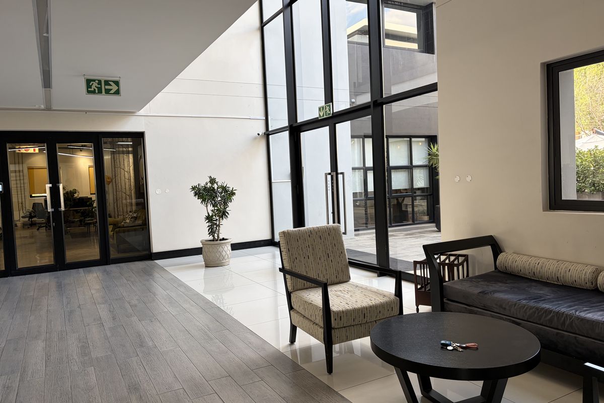 A bright, modern commercial lobby featuring floor-to-ceiling glass windows, tiled flooring, and a clean, professional aesthetic with direct access to office spaces.
