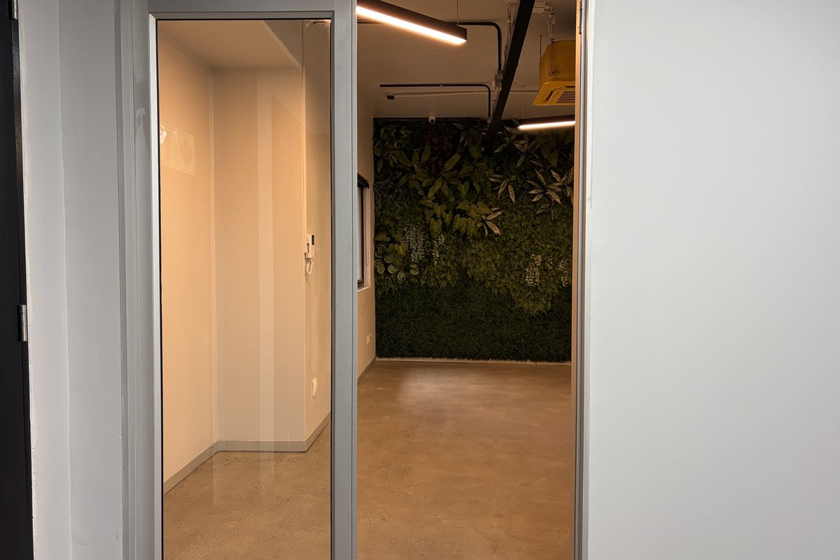 A modern office space featuring polished concrete floors, exposed industrial-style ceiling lighting, and a decorative vertical green wall feature.