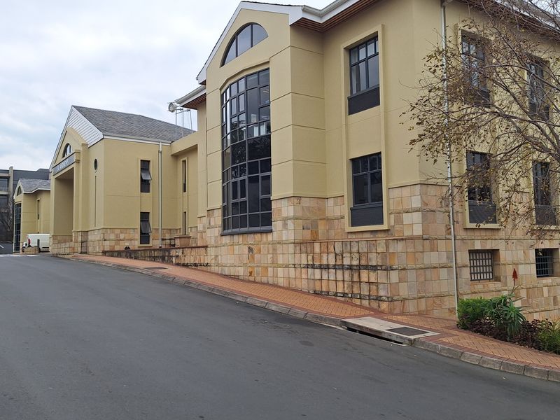 A professional office building exterior featuring a multi-story facade with stone cladding, large glass windows, and a paved driveway approach.