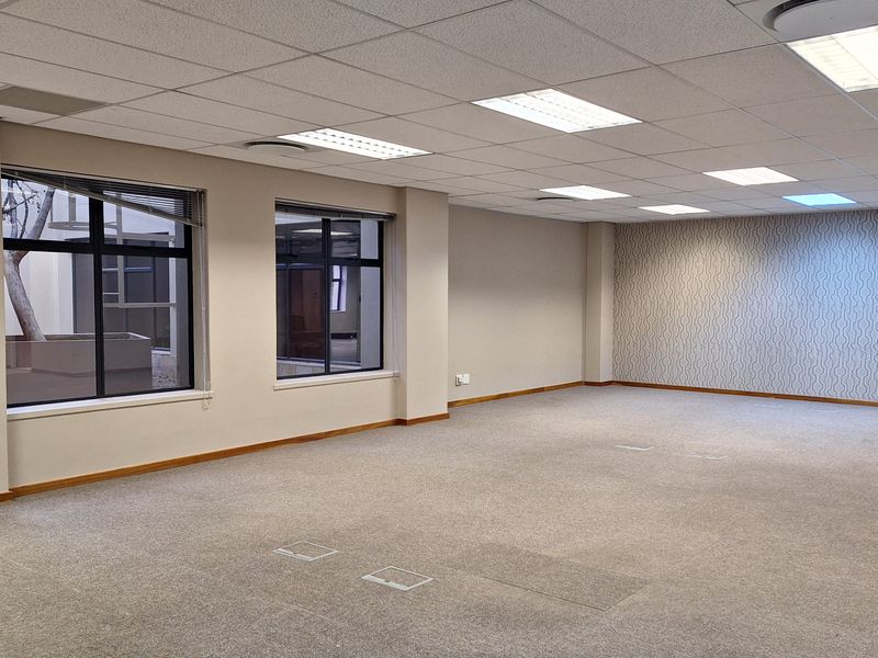 Spacious, open-plan office area featuring a suspended acoustic ceiling, recessed lighting, carpeted flooring, and large windows with integrated floor power access points.