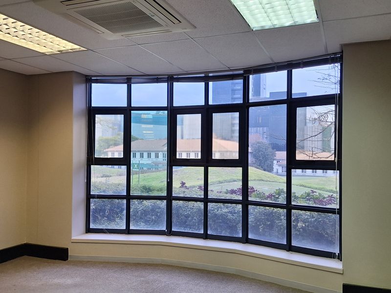 A vacant office space featuring large floor-to-ceiling windows with city views, recessed ceiling lighting, and integrated air conditioning unit.
